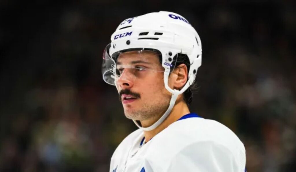 Action shot of the Toronto Maple Leafs' power play in full swing, showcasing players skillfully maneuvering the puck on the ice, with a key player absent from the lineup, while fans cheer passionately in the background.