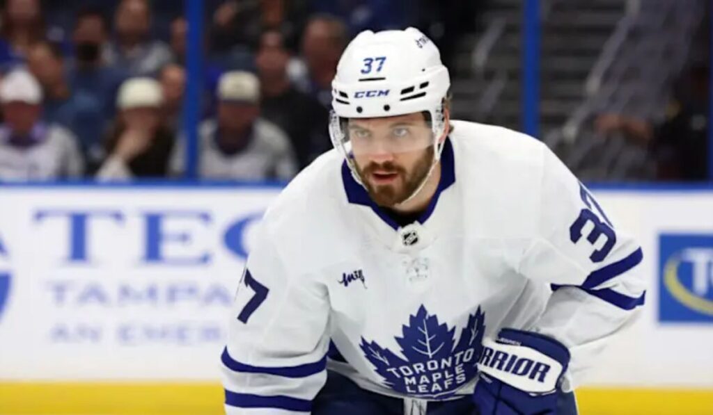 Maple Leafs defenseman in practice gear on the ice, looking contemplative, with a headline overlay reading 'Insider Report: Maple Leafs Defenseman's Debut in Doubt', emphasizing uncertainty about his upcoming debut.