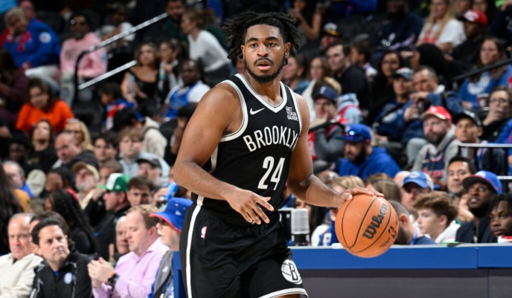 Image of a tense basketball game between the Brooklyn Nets and Memphis Grizzlies, showcasing players in action as they battle for the ball, with fans cheering in the background and a scoreboard displaying a close score.